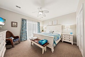 Ein Schlafzimmer mit Bett, Nachttischen, Schreibtisch, Stuhl, Deckenventilator und einem Fenster mit Vorhängen.