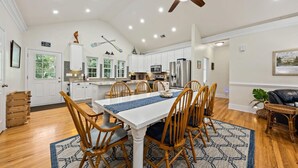 Una cocina amplia con armarios blancos, una isla central y un comedor con sillas de madera y una mesa blanca.