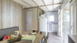 A compact kitchen with a microwave, a refrigerator, and a window with curtains. - ZEcamping familial espace aquatique animaux acceptés locatif TV 26m2 (Saint-Hilaire-de-Riez)