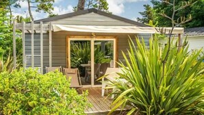 A small, single-story building with a covered patio area, a wooden deck, and a table and chairs set up for outdoor dining. - ZEcamping familial espace aquatique animaux acceptés locatif TV 26m2 (Saint-Hilaire-de-Riez)