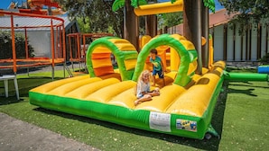 An inflatable play structure with slides and tunnels, surrounded by a fenced area with artificial grass. - ZEcamping espace aquatique animations locatif TV 26m2 5 pers (Saint-Hilaire-de-Riez)