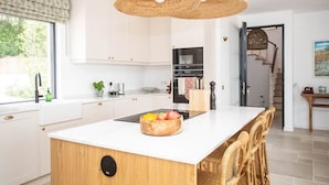 Een moderne keuken met witte kasten, een centraal eiland met een fruitschaal en rieten stoelen.