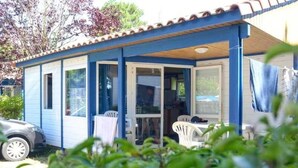 A small, single-story building with a blue exterior and a tiled roof. It has a covered patio area with a table and chairs. - ZEcamping animé parc aquatique chiens acceptés locatif 35m2 5 pers (Saint-Hilaire-de-Riez)