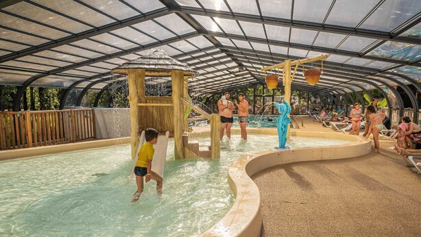 Et indendørs vandland med overdækket område, rutsjebaner og en swimmingpool.
