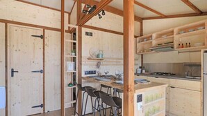 A wooden interior with a kitchen area, bar stools, and a refrigerator.