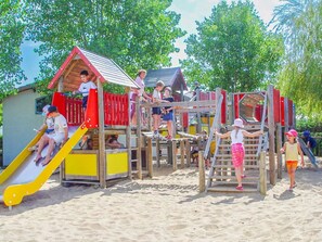 Ein Kinderspielbereich mit Rutsche, Klettergerüsten und einem kleinen Gebäude.