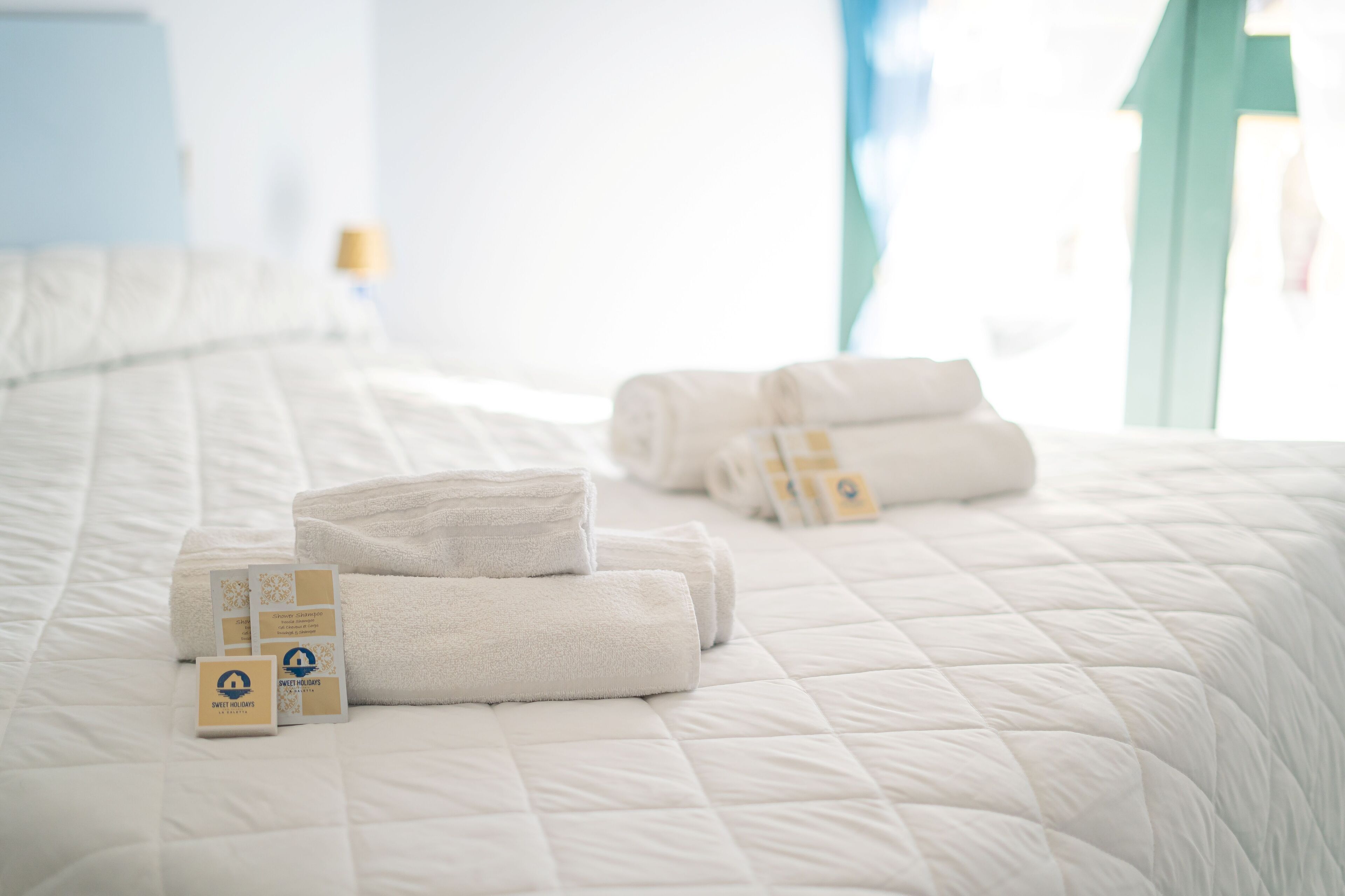 A neatly made bed with folded white towels and a set of cards on the bed.