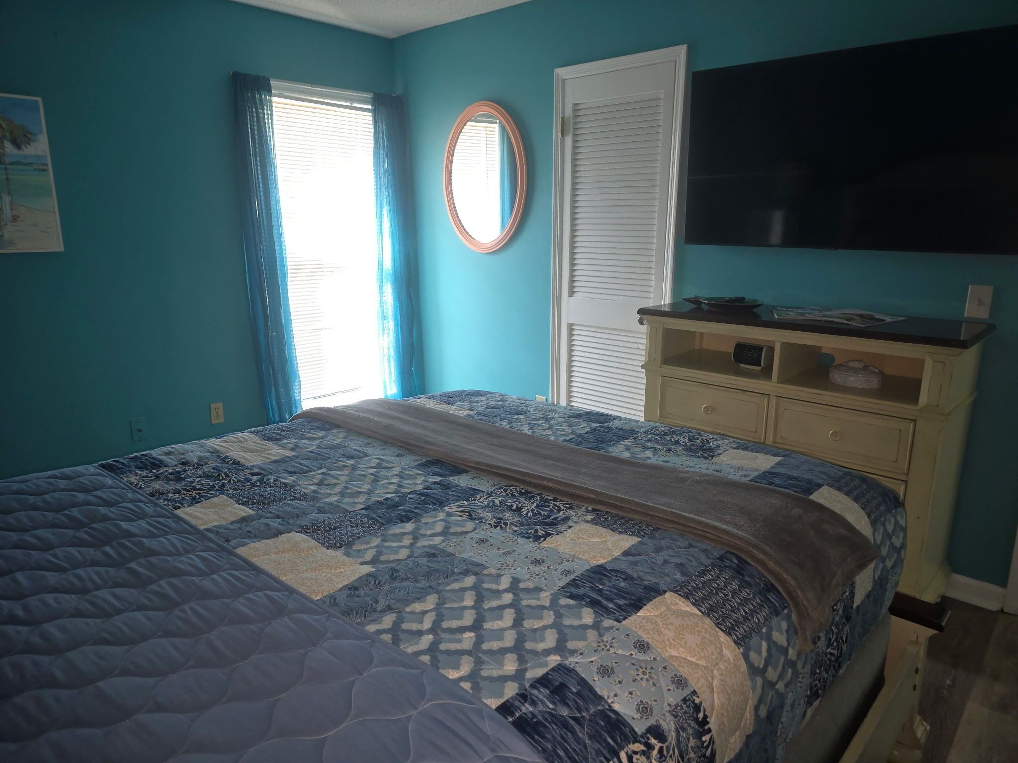 A bedroom with a bed, a dresser, a mirror, and a window with curtains.