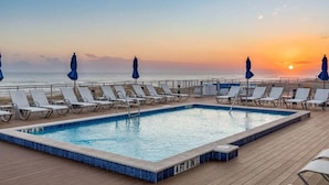 A poolside area with lounge chairs and umbrellas, overlooking the ocean at sunset. - Desired Lost Key community- walk to beach & golf course + tons of amenities! (Pensacola)