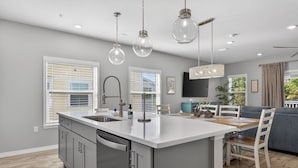 A modern kitchen with a central island, a dining area with a table and chairs, and a living area with a sofa and TV. - Desired Lost Key community- walk to beach & golf course + tons of amenities! (Pensacola)