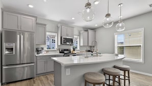 A modern kitchen with grey cabinets, stainless steel appliances, a white island with stools, and pendant lighting. - Desired Lost Key community- walk to beach & golf course + tons of amenities! (Pensacola)