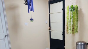 A hallway with a black door, a metal trash bin, a hanging plant, and a blue and white tiled floor.