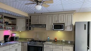 A kitchen with beige cabinets, a microwave, an oven, a refrigerator, and a ceiling fan.