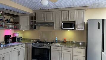 A kitchen with beige cabinets, a microwave, an oven, a refrigerator, and a ceiling fan.
