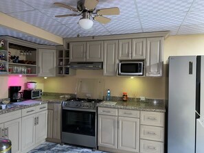 Una cocina con armarios color beige, un microondas, un horno, un refrigerador y un ventilador de techo.