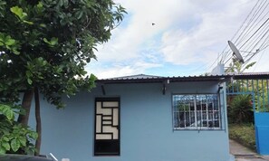 A small, single-story building with a blue exterior, a window with decorative metal bars, and a satellite dish on the roof.