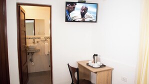 A hotel room with a wooden door leading to a bathroom, a small wooden table with a chair, and a television mounted on the wall. - san blas plaza hotel (Cusco)