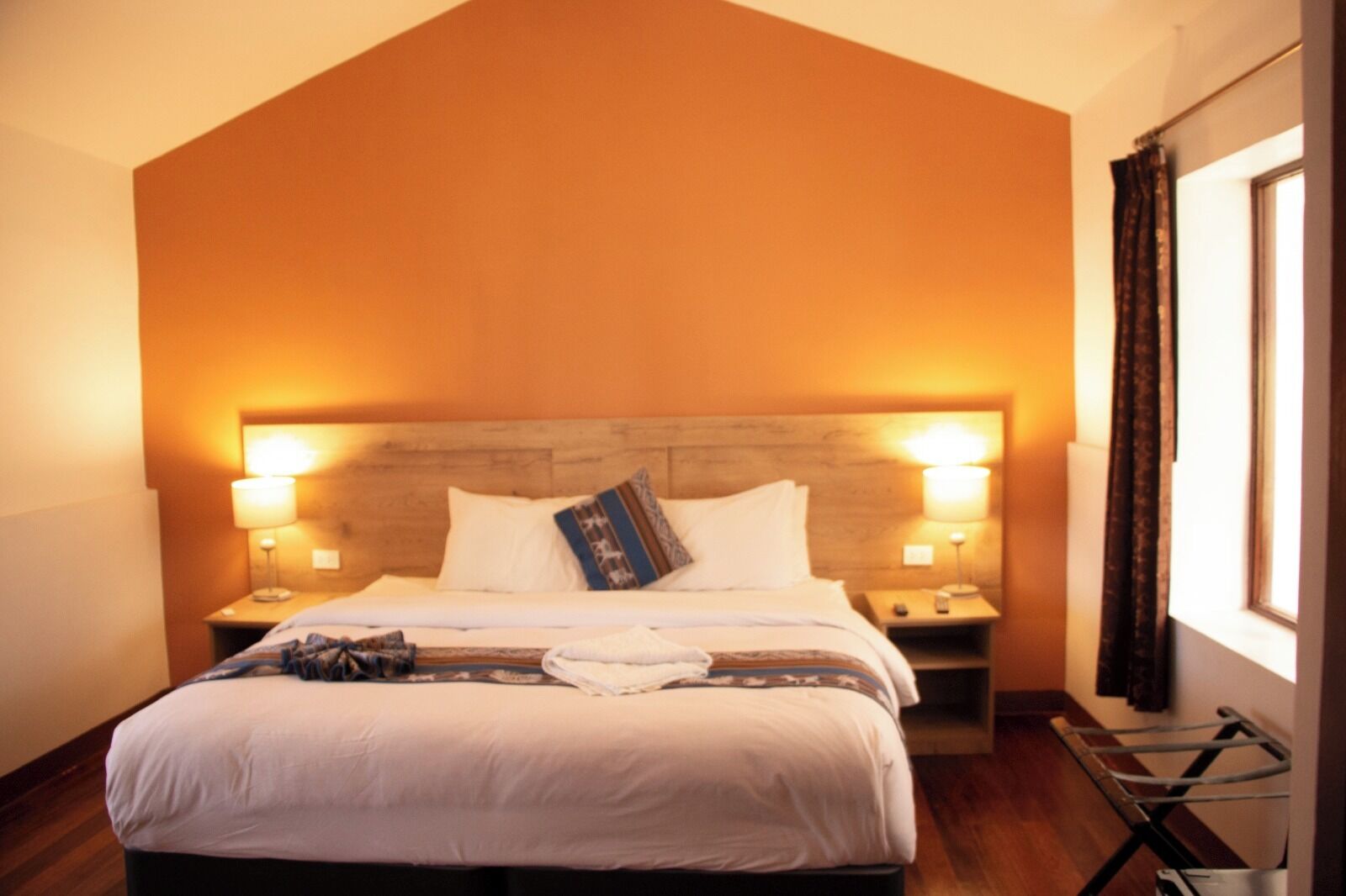 Una habitación de hotel con una cama grande, dos mesitas de noche, un cabecero de madera y una ventana con cortinas.