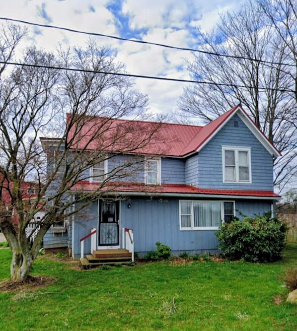 A two-story house with a red roof, a front porch, and a small front yard.