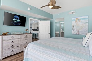 Une chambre à coucher avec un lit, une commode, un ventilateur de plafond, une télévision et un tableau.