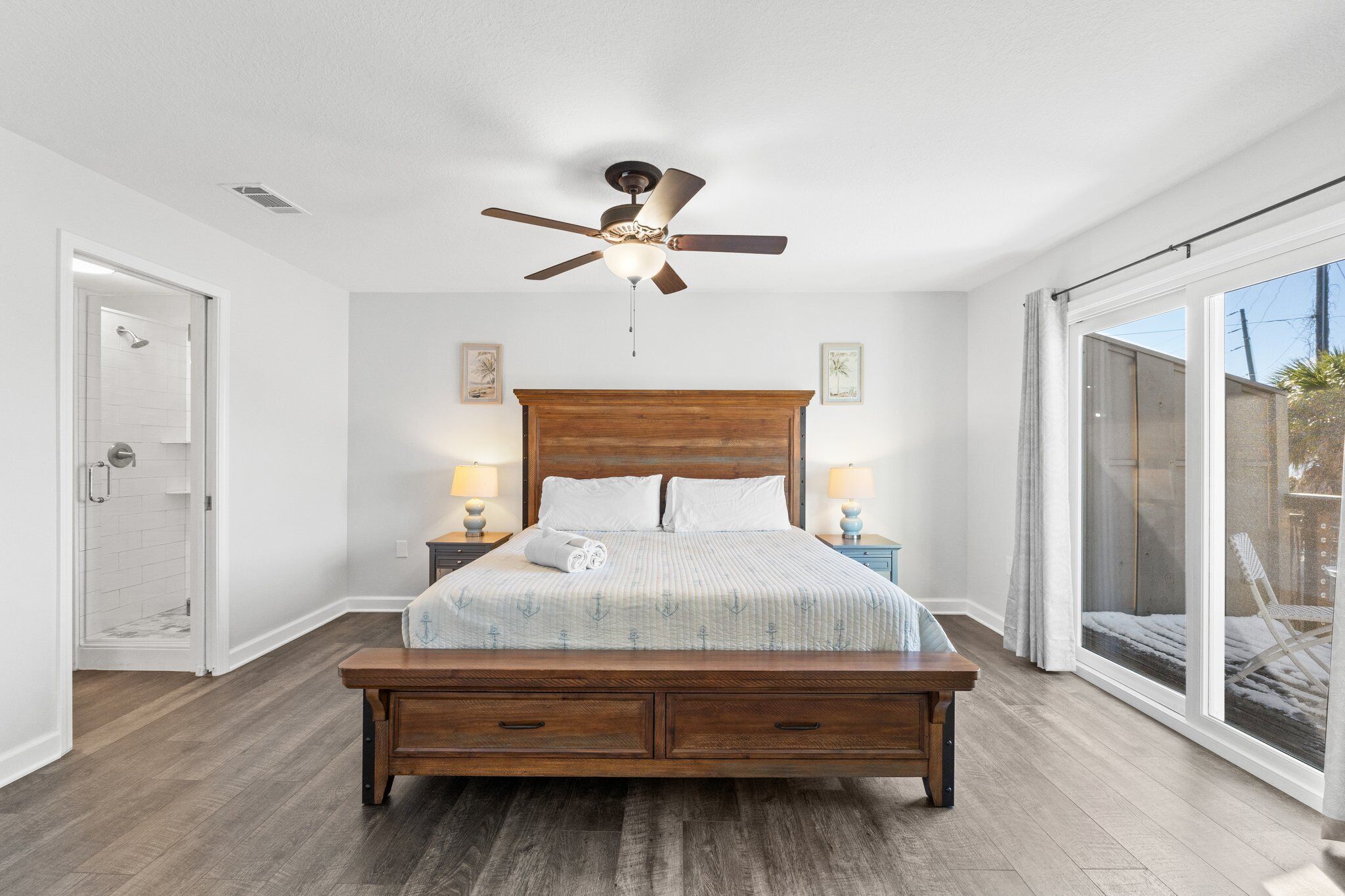 A bedroom with a wooden bed, a ceiling fan, a nightstand with a lamp, and a sliding glass door to the outside.