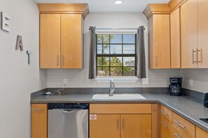 A kitchen with wooden cabinets, a stainless steel dishwasher, a sink, and a window with blinds. - Panhandle Paradise, Waterfront, 2 Dog Friendly in Fort Walton Beach. Free Activities Included! (Fort Walton Beach)