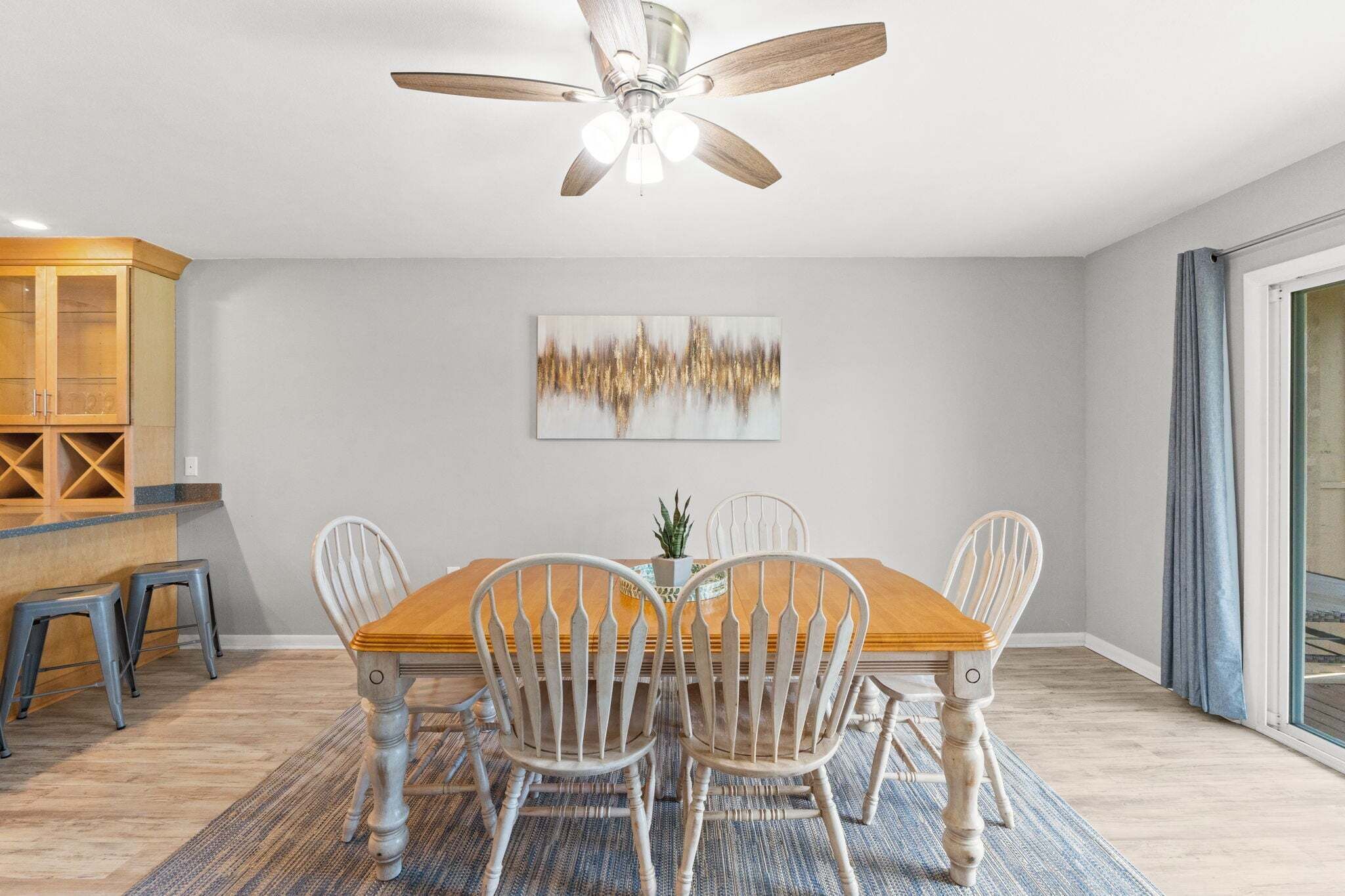 A dining area with a wooden table and chairs, a ceiling fan, a cabinet, and a painting on the wall.