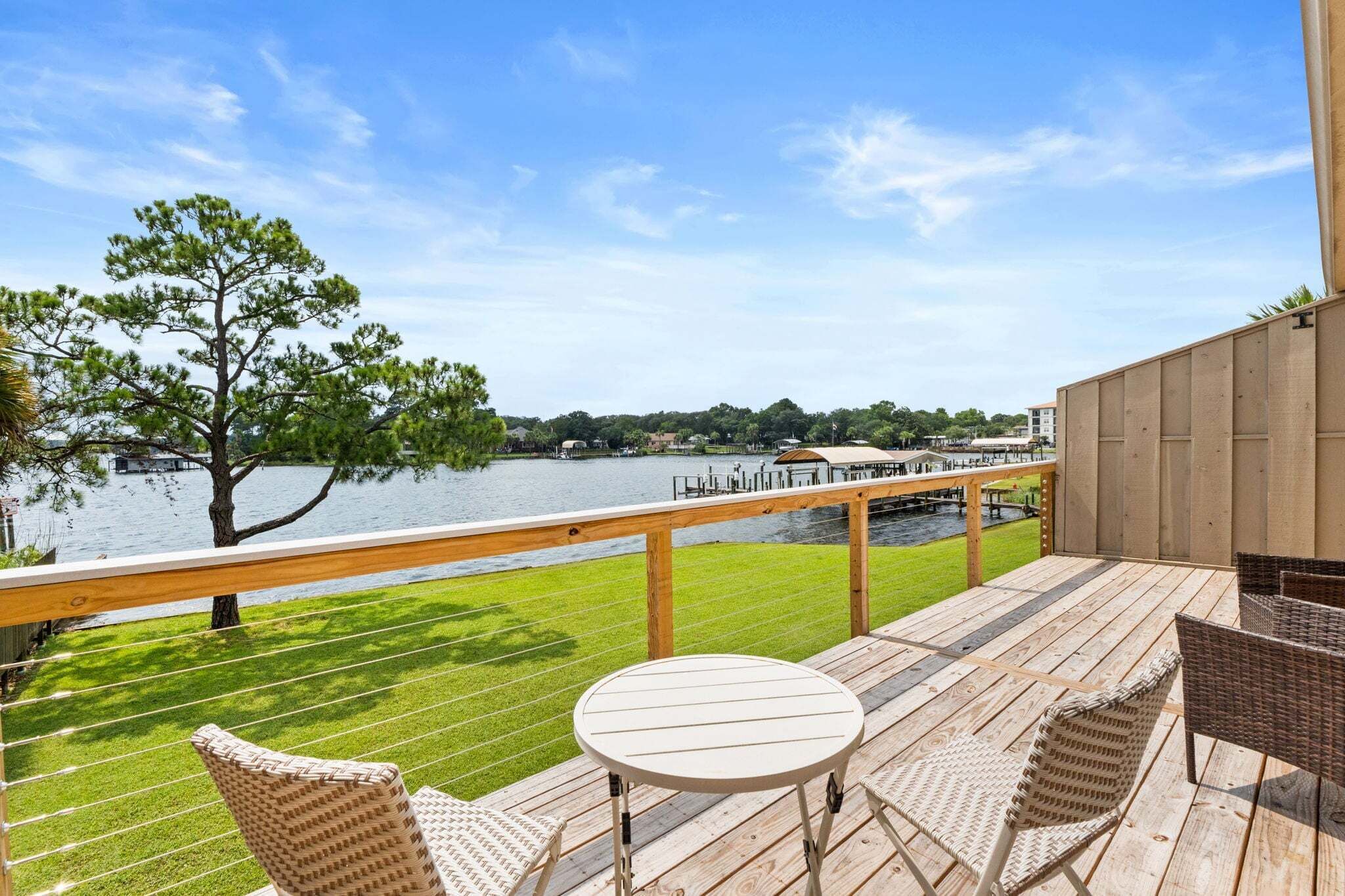 Une terrasse offrant une vue sur un lac, un arbre et une côte lointaine parsemée de bâtiments.