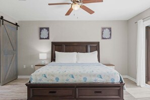 A bedroom with a bed, nightstands, a ceiling fan, and two wall-mounted decorative items. - Panhandle Paradise, Waterfront, 2 Dog Friendly in Fort Walton Beach. Free Activities Included! (Fort Walton Beach)