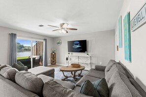 A living room with a sofa set, a coffee table, a television, and a view of a body of water through a sliding door. - Panhandle Paradise, Waterfront, 2 Dog Friendly in Fort Walton Beach. Free Activities Included! (Fort Walton Beach)
