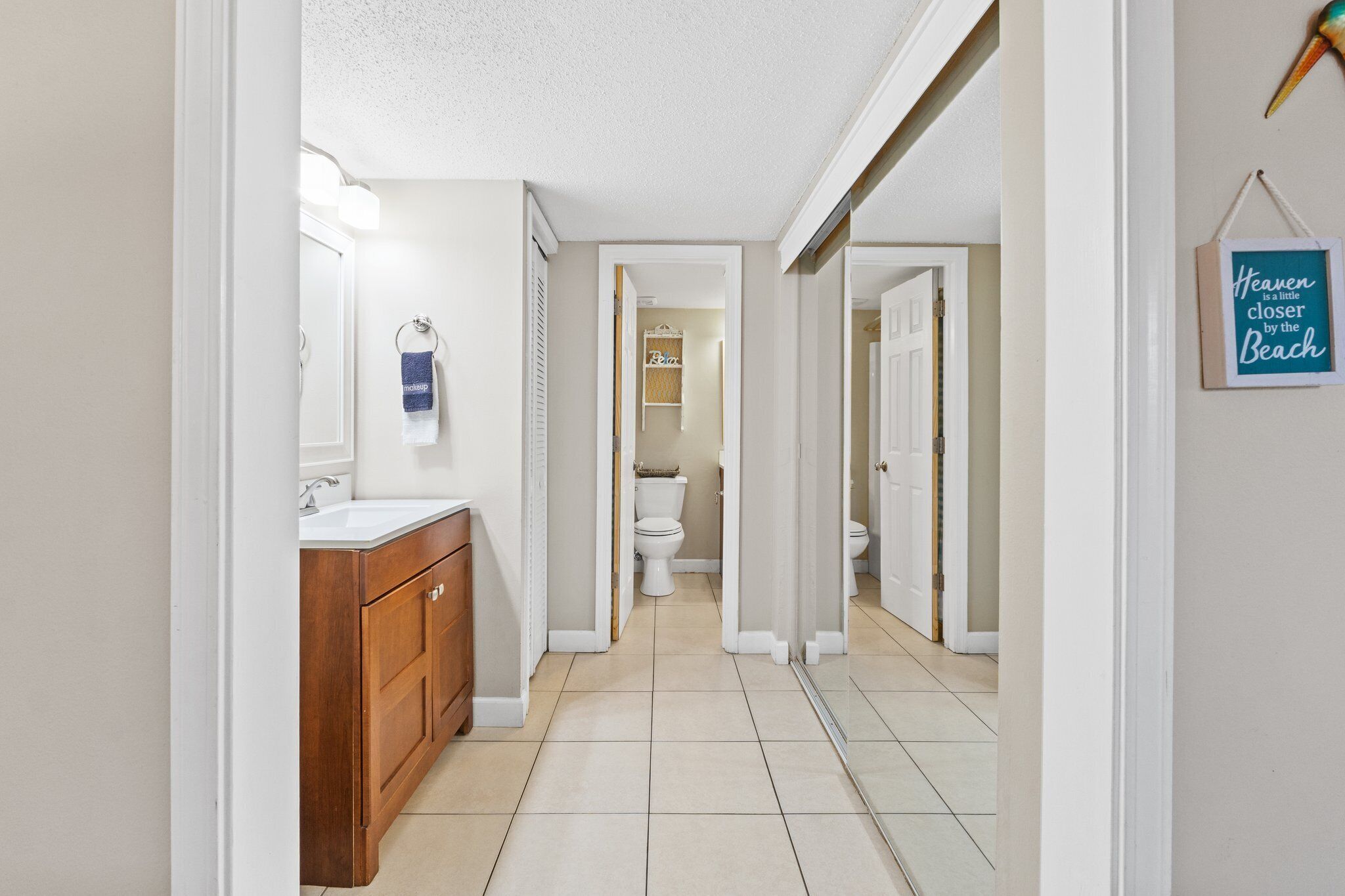 A narrow hallway with a wooden vanity and a white sink, leading to a bathroom with a toilet and a shower area.
