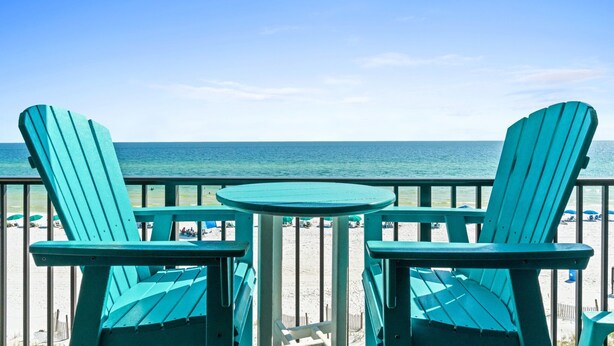 A balcony with two green Adirondack chairs and a small round table, overlooking a beach with umbrellas and people. - Beach Front, "Resting Beach Face” 4006 Free Activities Included (Fort Walton Beach)