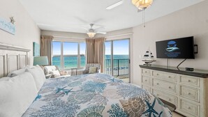A bedroom with a bed, a ceiling fan, a TV, a dresser, and a view of the ocean. - Beach Front, "Resting Beach Face” 4006 Free Activities Included (Fort Walton Beach)