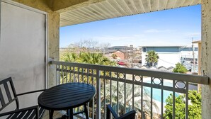 Un balcon avec une table et des chaises, donnant sur une piscine et un quartier résidentiel.