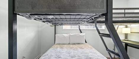 A compact room with a bunk bed, a small desk with a lamp, and a window providing natural light.