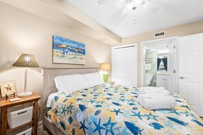 A bedroom with a bed, a nightstand, a lamp, a painting, and a door. - Beachfront Condo with Pool, Hot Tub & Free Beach Service – Perfect for Families! (Fort Walton Beach)