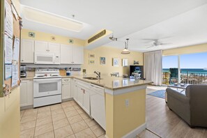 Une cuisine compacte avec des appareils électroménagers blancs, un coin repas offrant une vue sur l’océan et un balcon avec une chaise.
