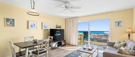 Un salon comprenant un coin repas, un téléviseur et un balcon avec vue sur l’océan.