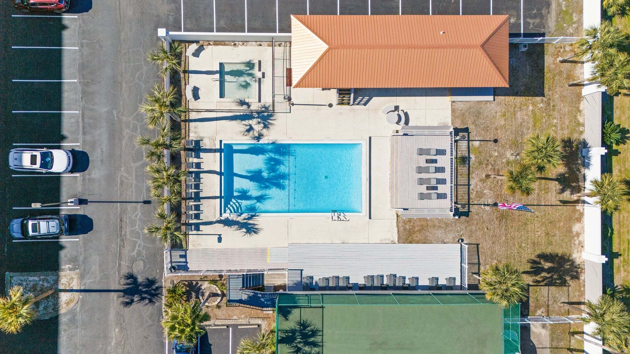 Luchtbeeld van een hotel met een zwembad, ligbedden en een tennisbaan.