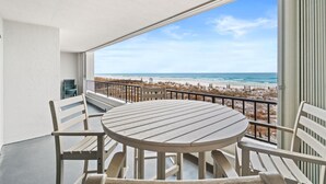 A balcony with a round table and chairs, overlooking a beach with the ocean and a clear sky. - Beachfront~Beach Service~Stunning Views~Free Activities~Surf Dweller 210 (Fort Walton Beach)