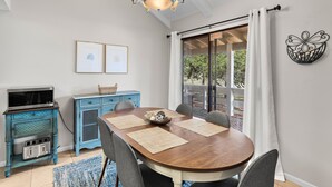Een eethoek met een houten tafel, stoelen, een kroonluchter, een blauwe kast en uitzicht door een glazen deur.