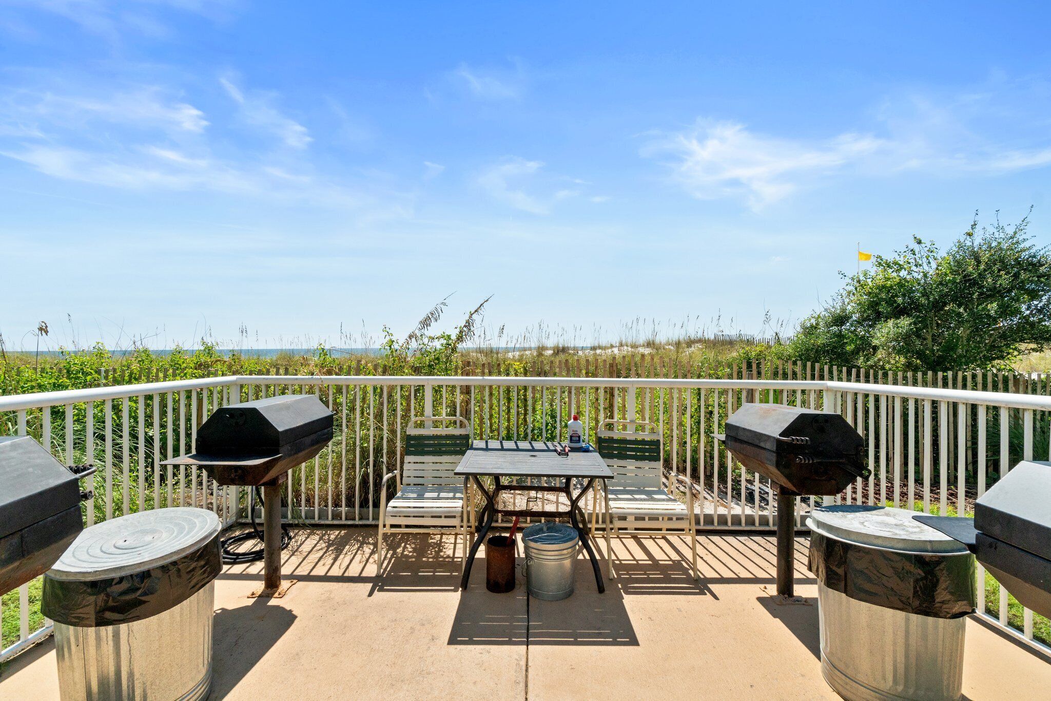 A balcony with a table, two grills, and two trash cans.
