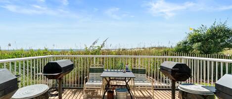 A balcony with a table, two grills, and two trash cans.