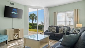 Una sala de estar con una mesa de centro de vidrio, un sofá, un televisor montado en la pared y vistas al exterior a través de un gran ventanal corredero.