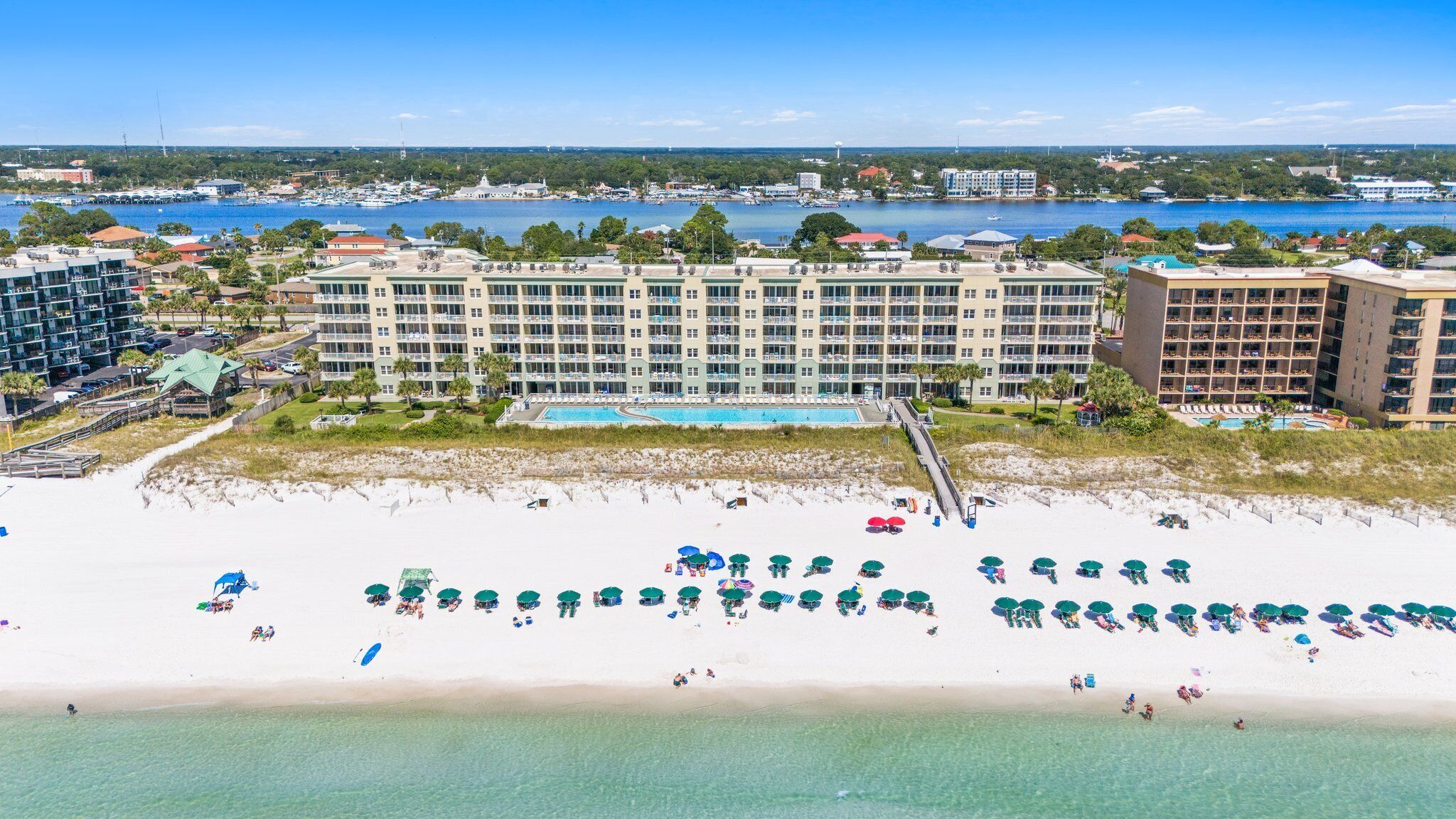 A beachfront hotel with multiple buildings, a swimming pool, and a sandy beach with umbrellas.