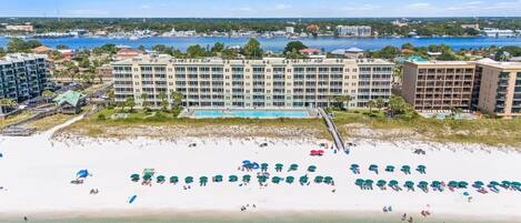 A beachfront hotel with multiple buildings, a swimming pool, and a sandy beach with umbrellas.