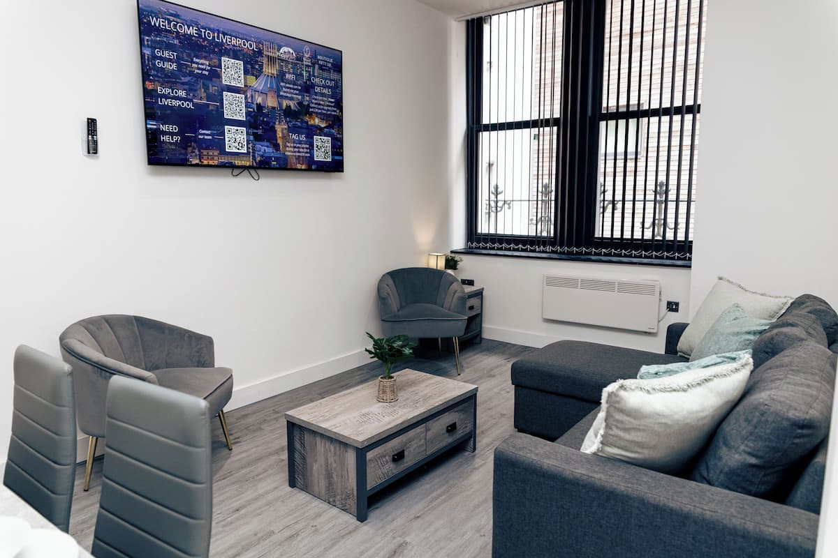 A modern living room with a large window, grey furniture, a mounted TV, and a remote control on the wall.