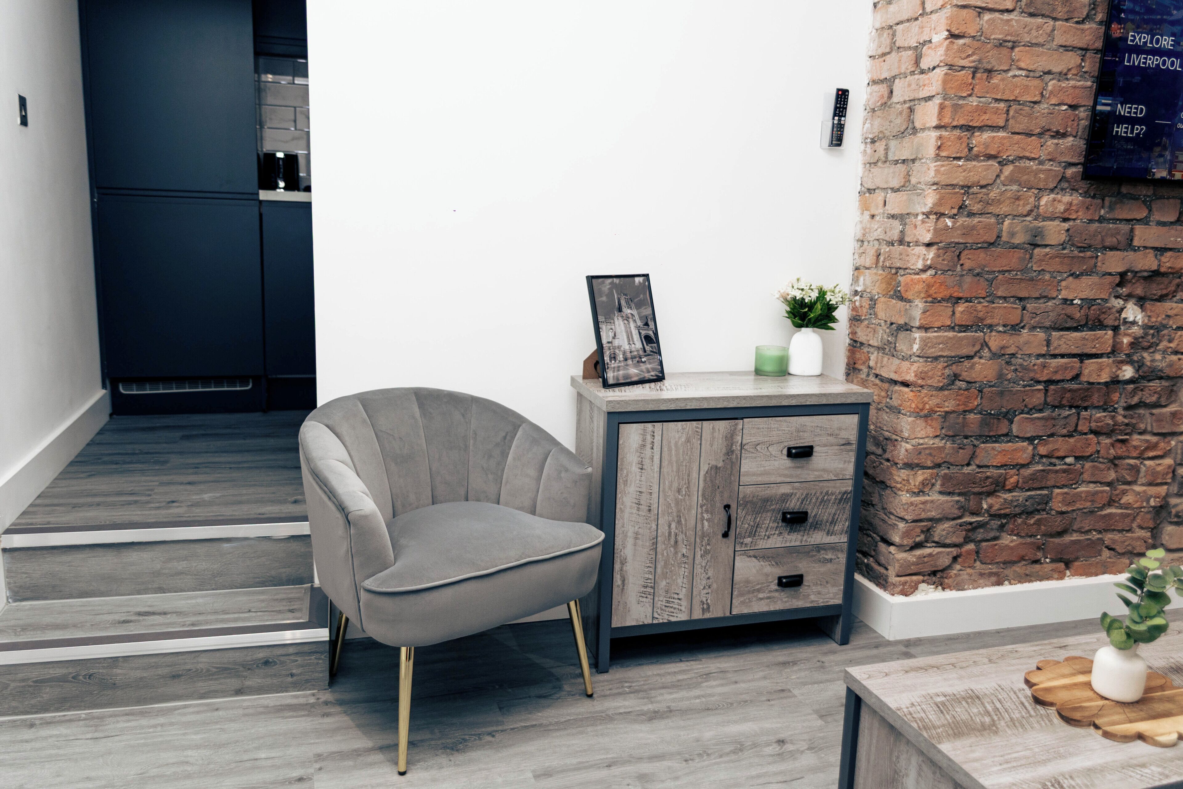 Een modern interieur met een grijze fauteuil, een houten kast en een bakstenen muur.