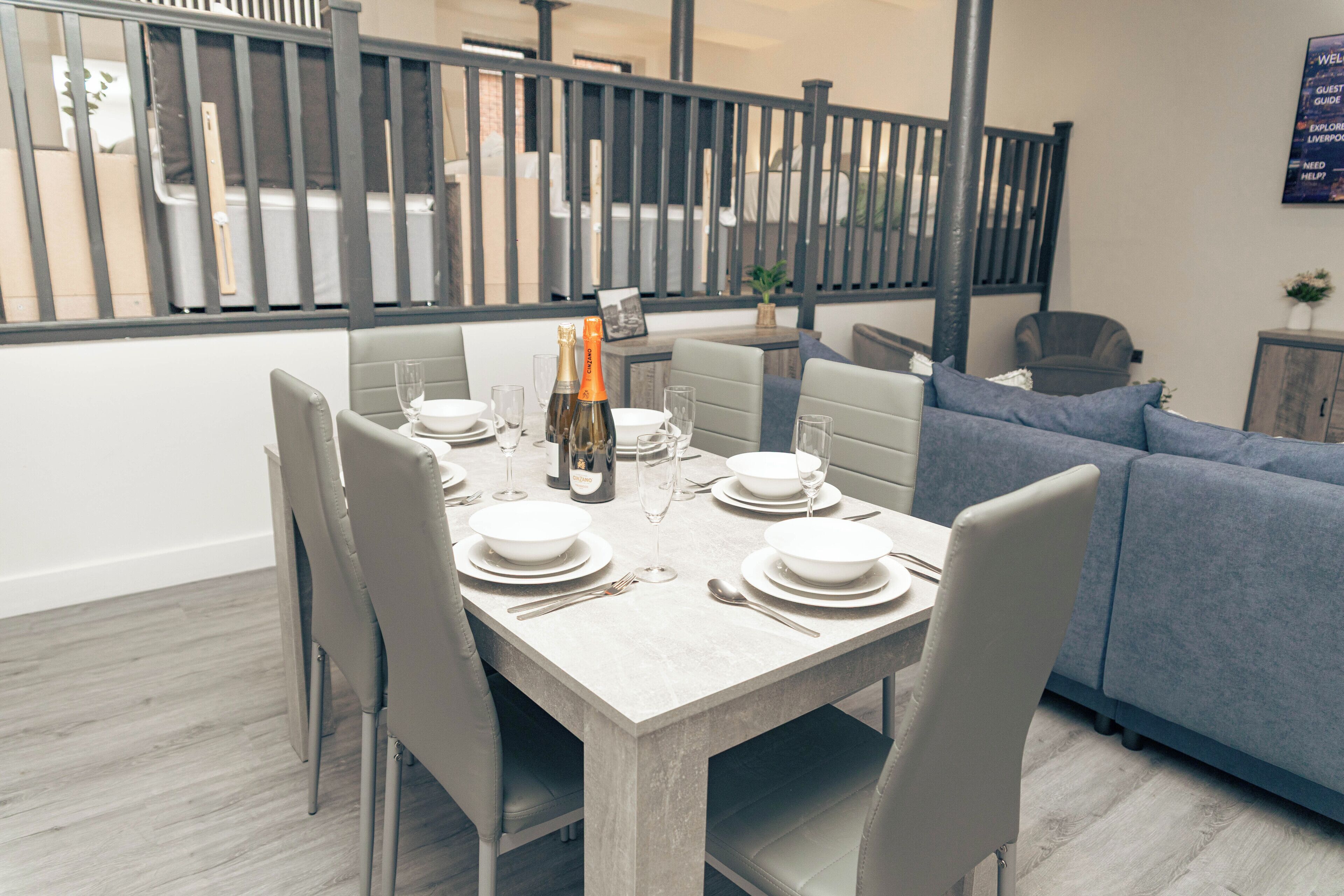 A dining area with a table set for four, a sofa, and a view of a balcony with a railing.