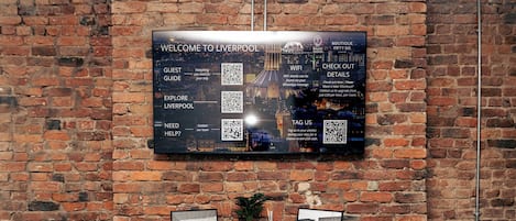 En digital skärm som är monterad på väggen och visar ett välkomstmeddelande, QR-koder och en vy över Liverpool.